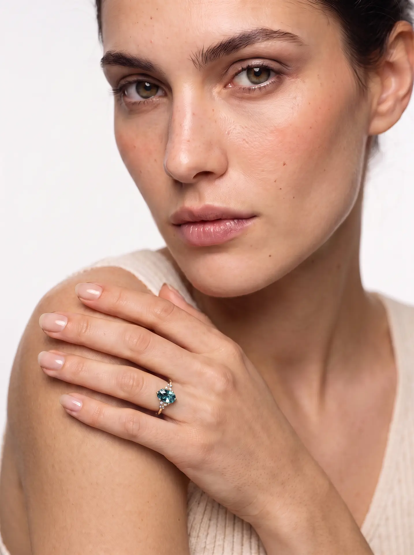 A close-up lifestyle photo of a gold oval sapphire cluster engagement ring worn on a woman's hand.