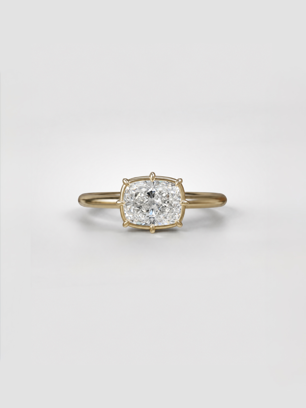 East-West elongated cushion lab-grown diamond solitaire ring with sleek claw prongs and a collet setting on a gold wire band.